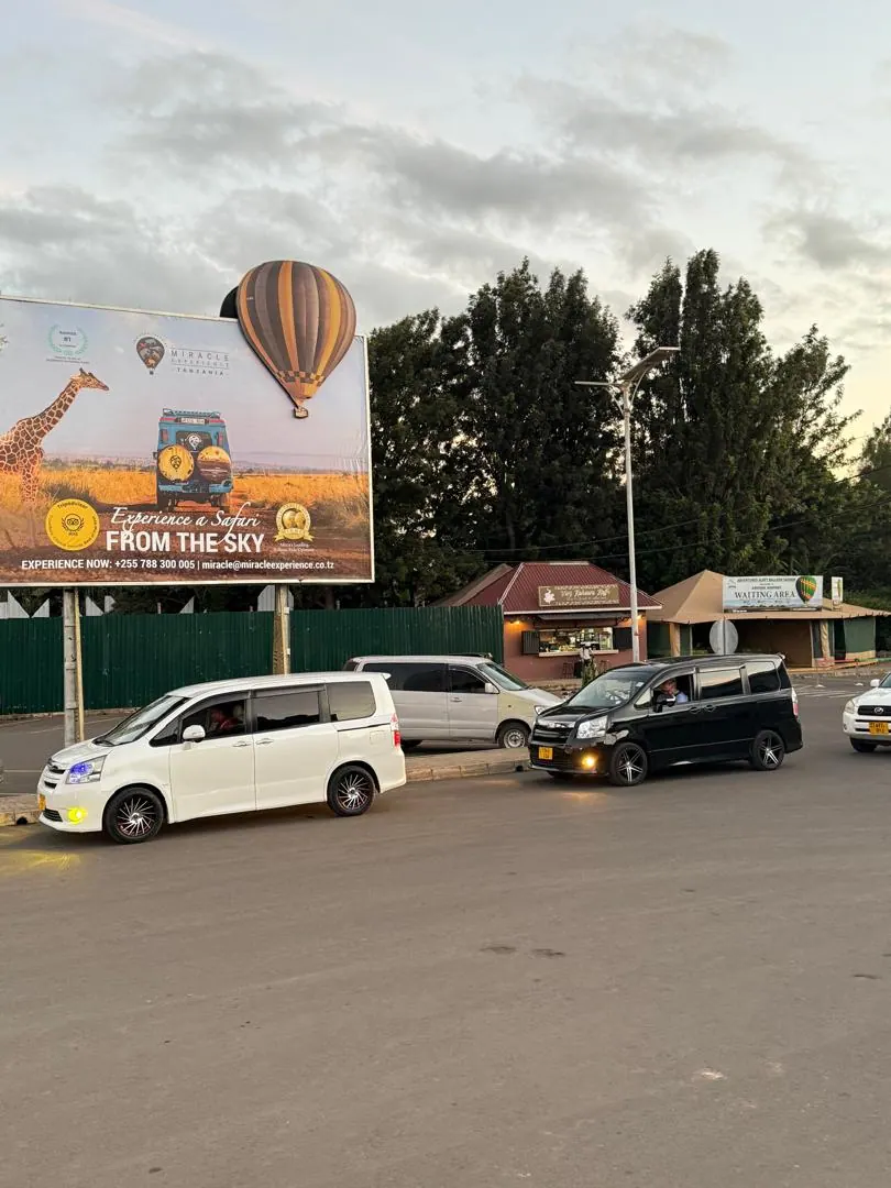 An Arusha street at dusk, cars passing a roadside billboard
