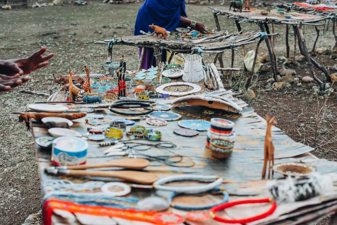 Beaded jewellery, carved spoons and painted bowls laid out on a table at the boma
