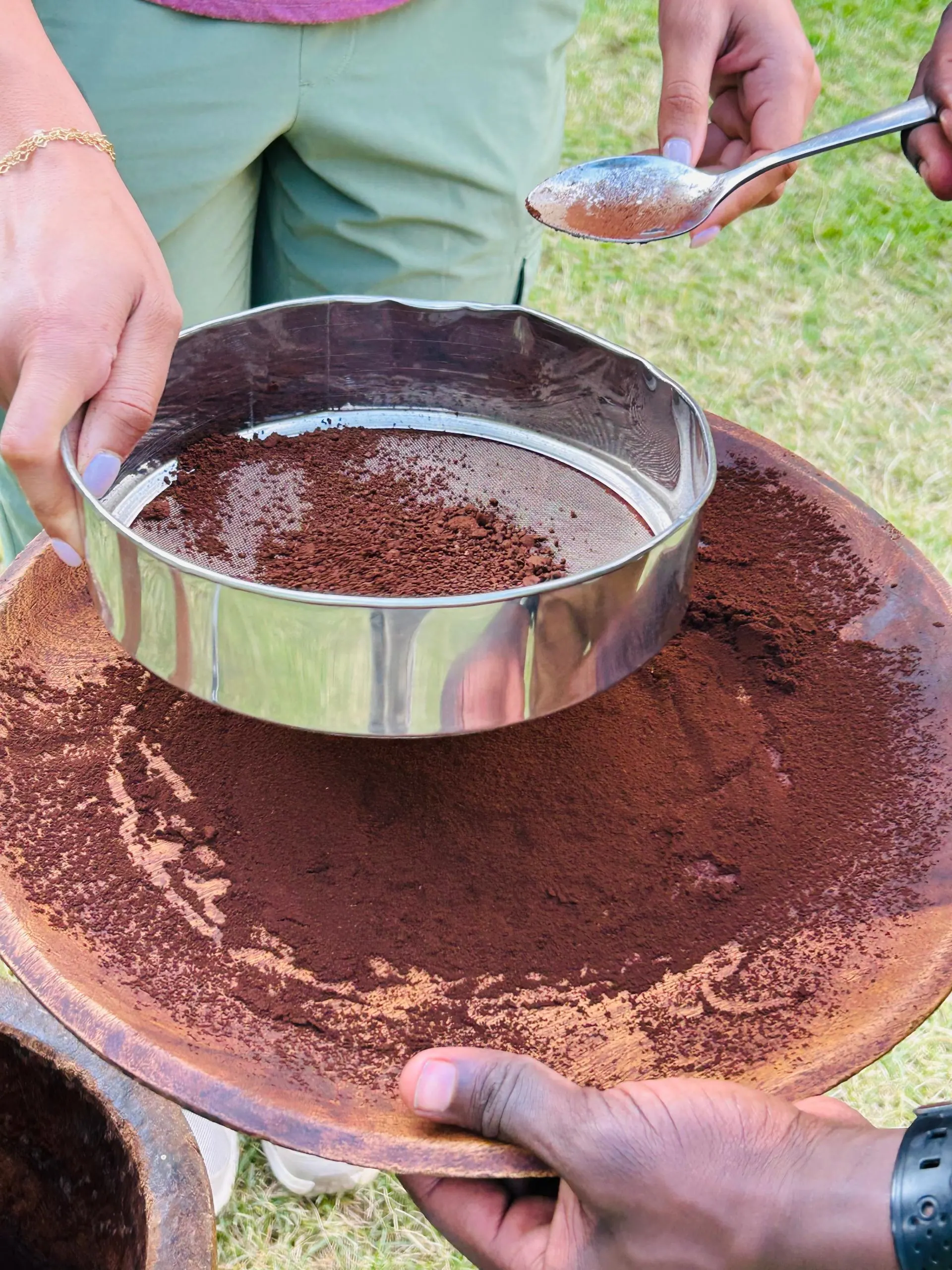Freshly ground coffee being sifted through a sieve into a wooden bowl