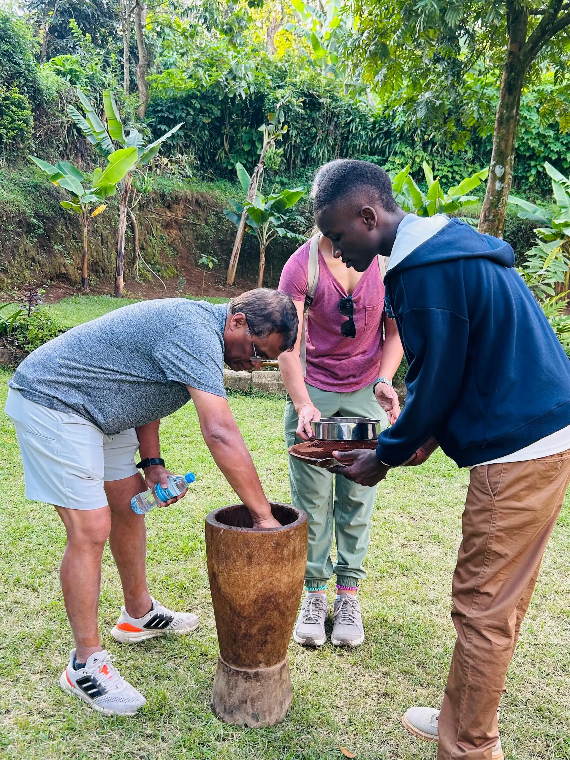Visitors pounding roasted coffee beans in a tall wooden mortar