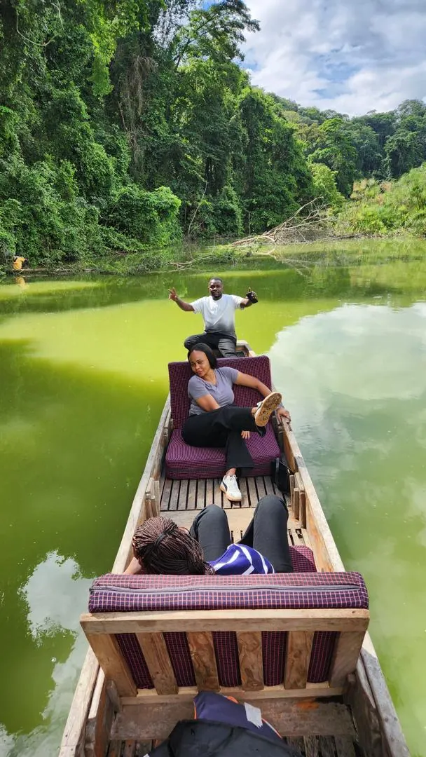 A guide standing at the bow of a canoe on the green water of Lake Duluti below the forested crater wall