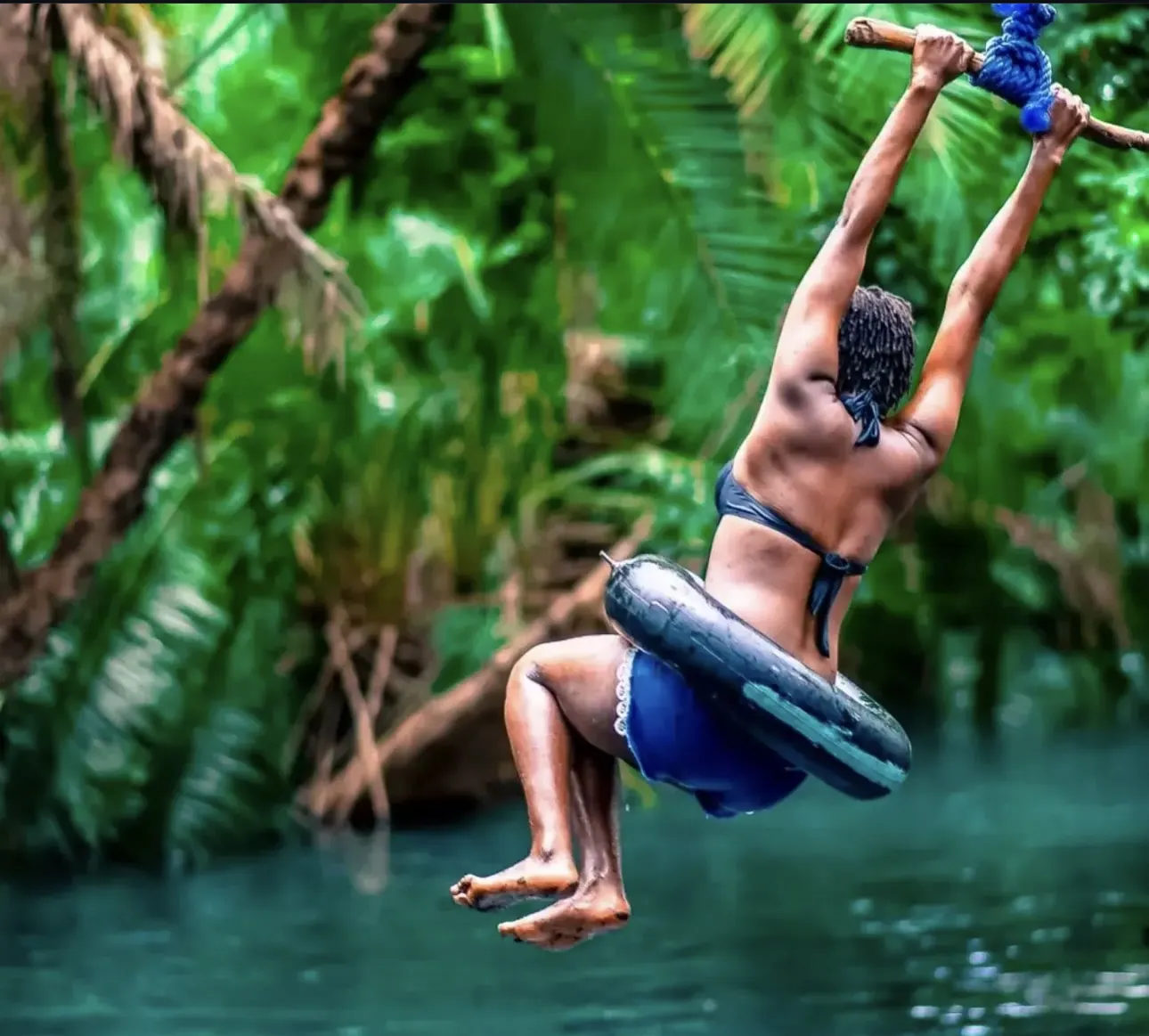 A swimmer swinging out on a rope over the clear turquoise water of the springs, forest all around