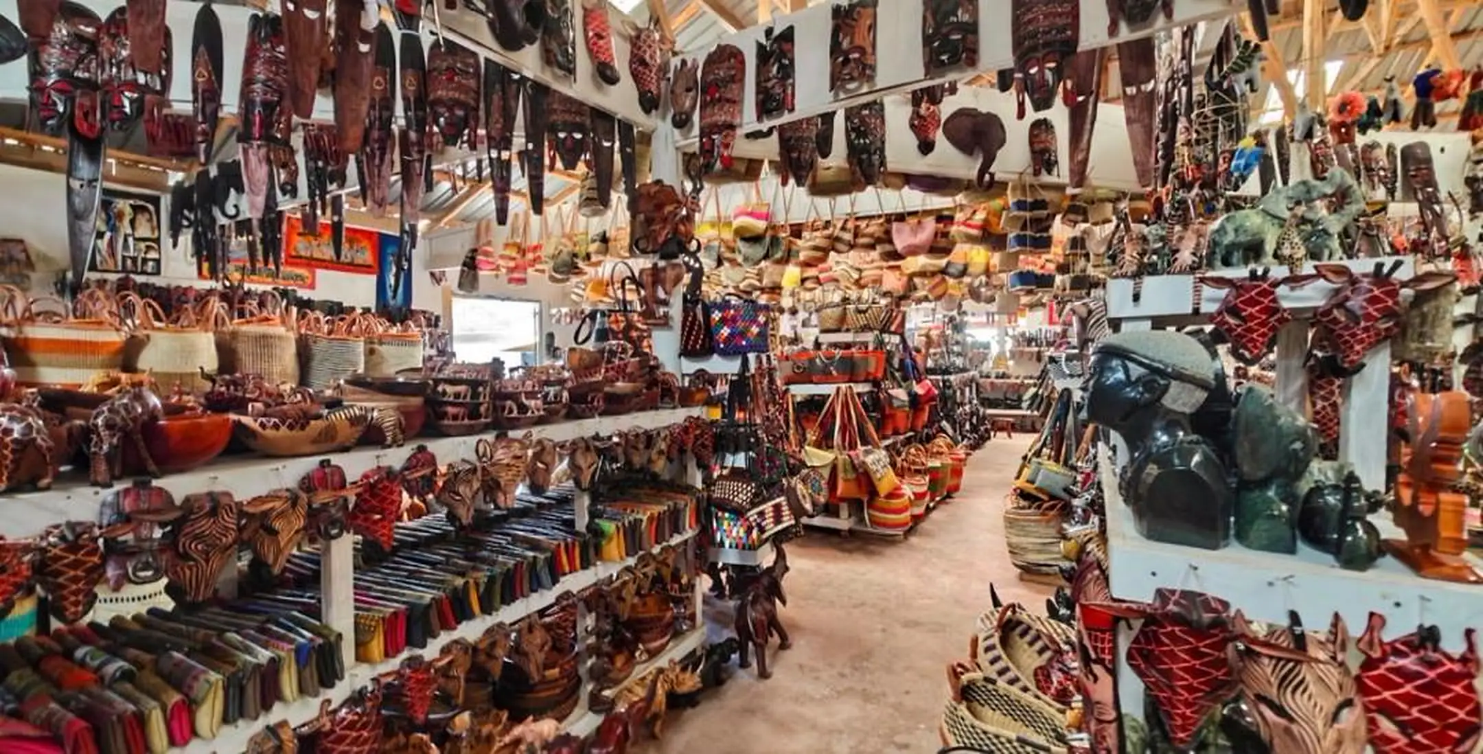 Inside a covered craft hall: masks, baskets, bags and carvings on the shelves and hanging from the roof